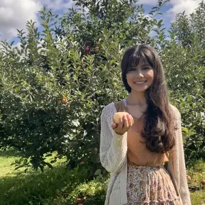 Gloria Parrales ’24, smiling, holds an apple in an orchard