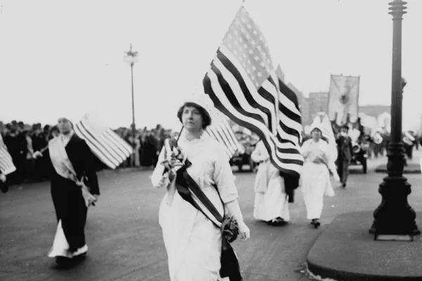 A woman in white carrying an American flag in the 1913 parade on Washington