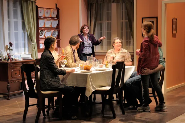 Six actors on stage around a dinner table