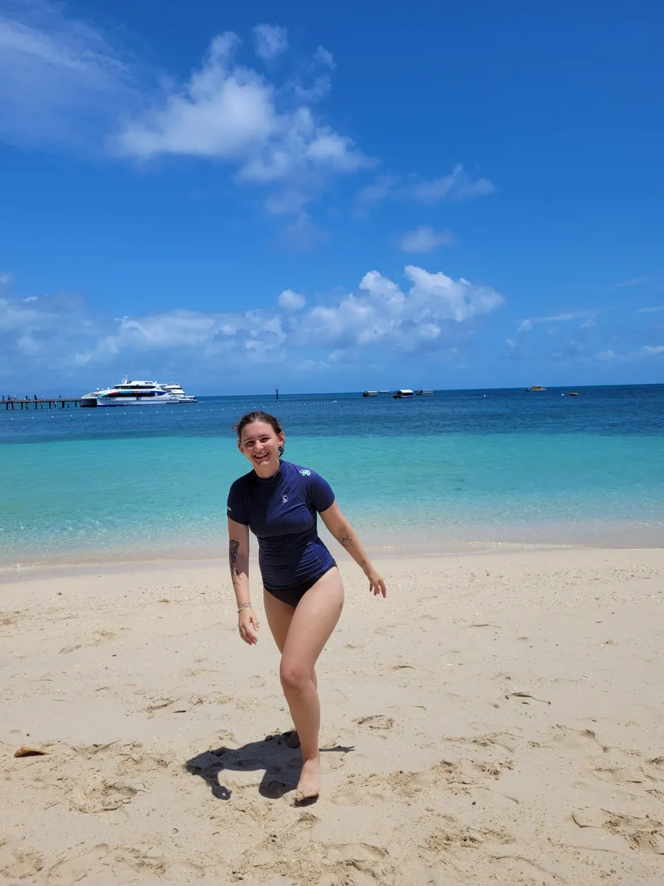 Leah Harries ‘24 in a navy swim suit next to tropical blue waters and a blue sky