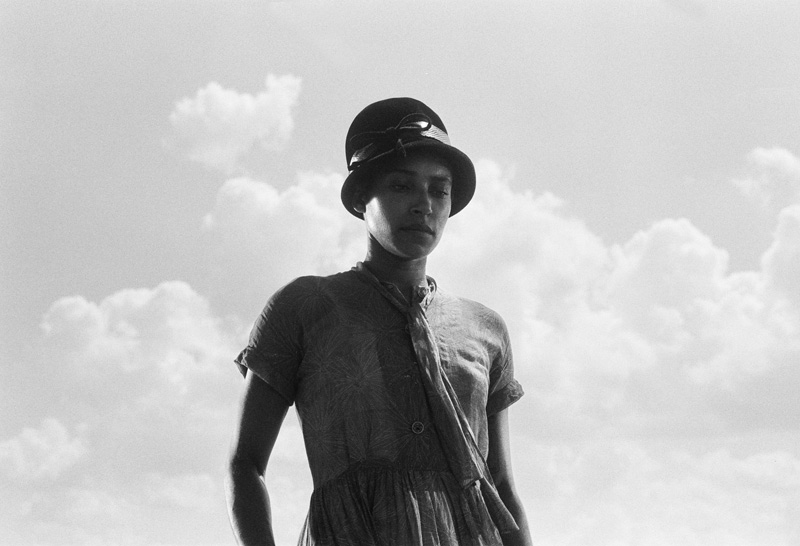 Black woman in a dress and cloche looking down, surrounded by clouds