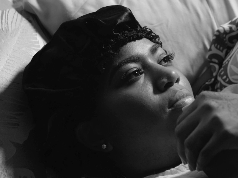 Black woman lying in bed, looking thoughtfully to the left