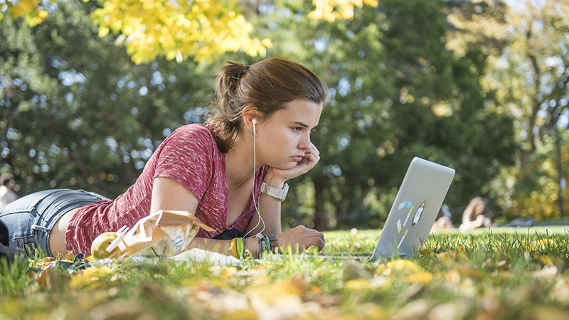 Student lying on the grass looking at her laptop screen