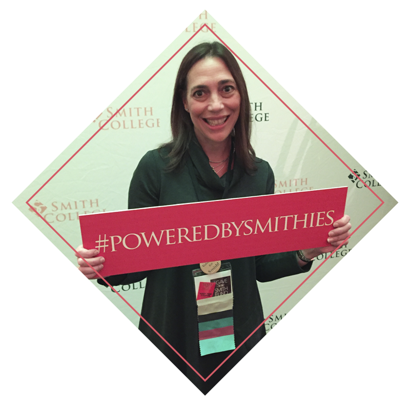 Photo of Dana Maze Ehrlich smiling and holding a sign that says Powered by Smithies
