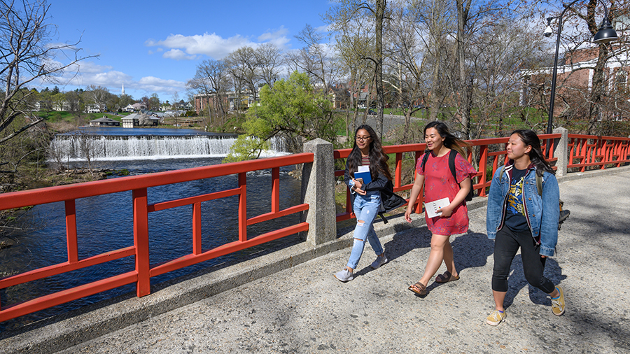 Three students walking across a bridge
