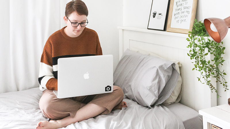 Student sitting on bed studying with laptop