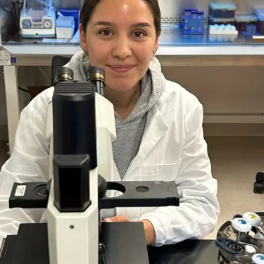 Mary Ann Martinez ’25J in a lab coat in front of a microscope