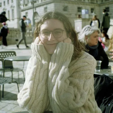 Sarah (SJ) Waring ‘24 in a white sweater, smiling, with her head in her hands