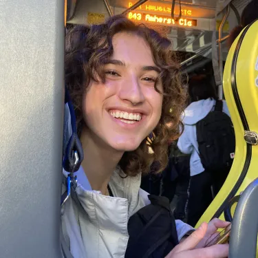 Pria Parker ’25 looks out of a doorway, smiling, with a yellow cello case