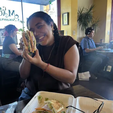 Kim Estrada laughing and holding up a sandwich in a restaurant