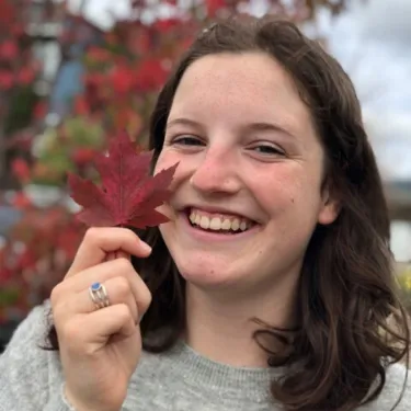 Iliana Pliska-Bloch smiling holding an autumn leaf