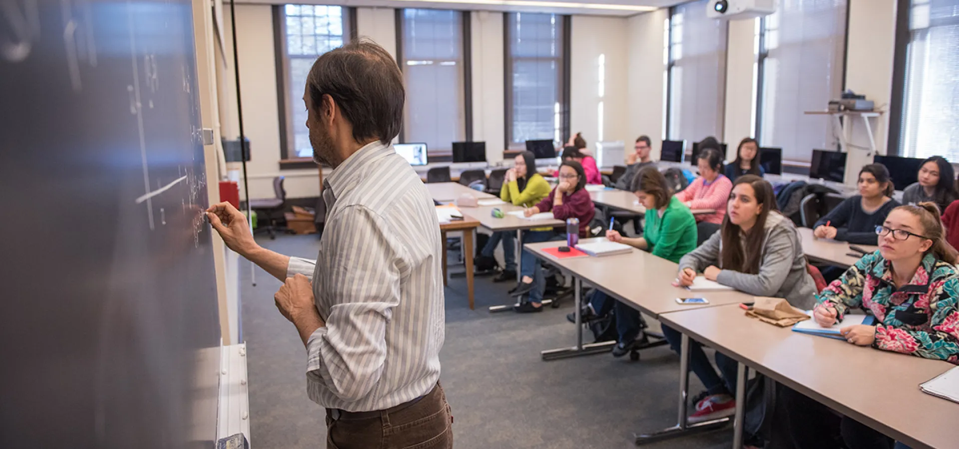 Pau Atela writes math problems on blackboard to classroom of Smith College students