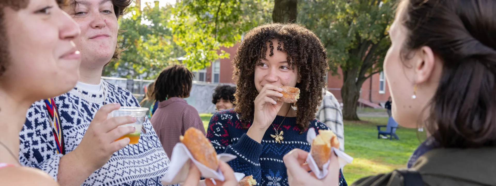 A student enjoys an apple cider donut and smiles at a friend on Mountain Day 2025