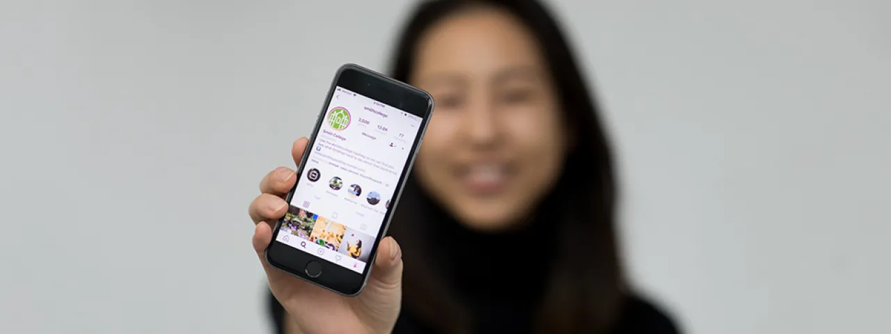 Student holding a cell phone displaying a Smith College's social media page