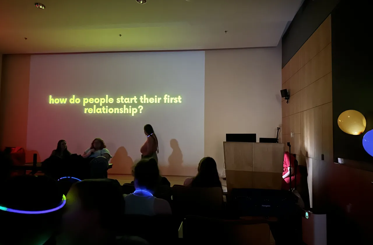 Sex in the Dark education event with lights off and a screen with yellow letters how do people start their first relationship
