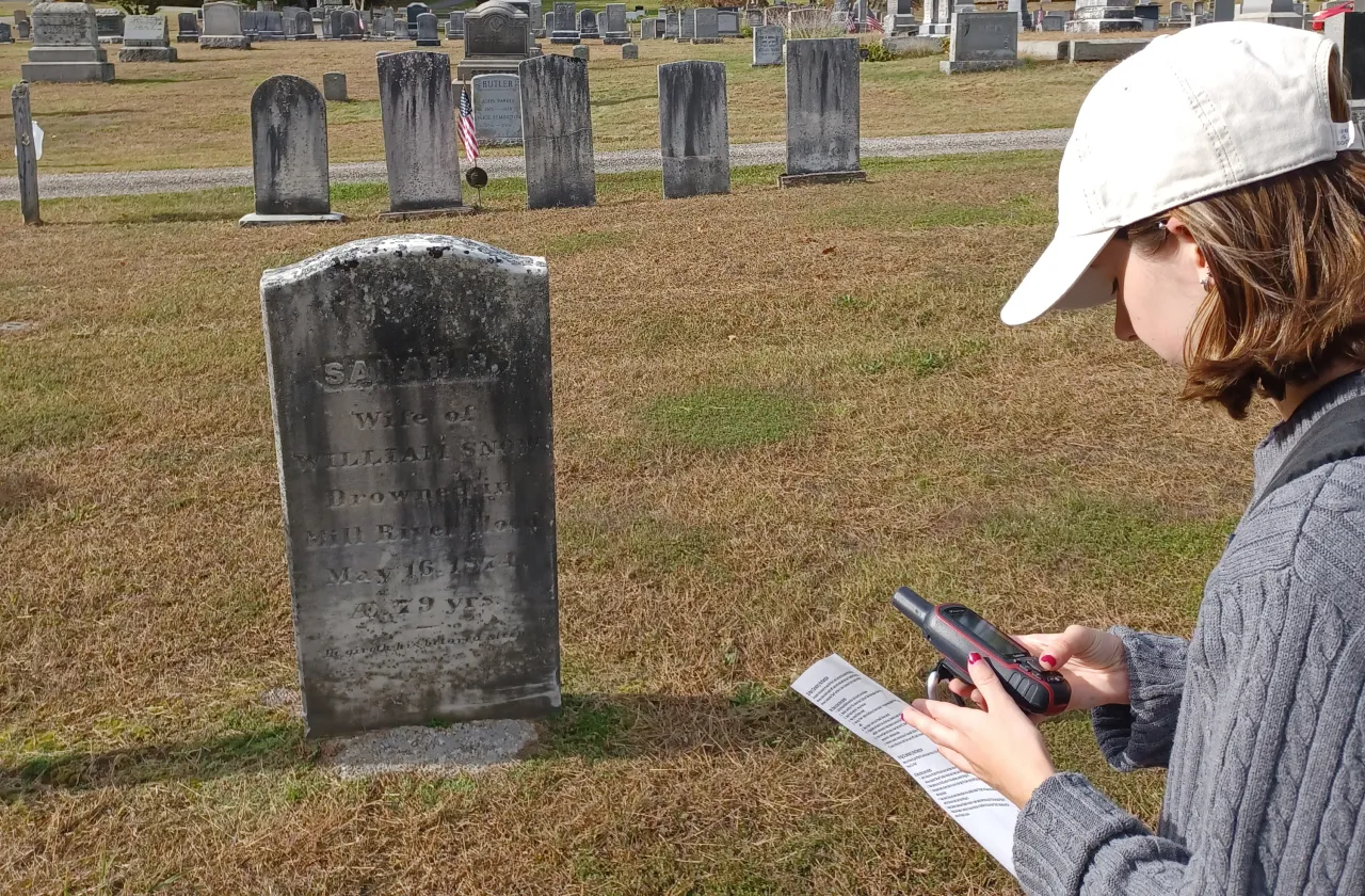 A student holds a tracking device in a cemetery.