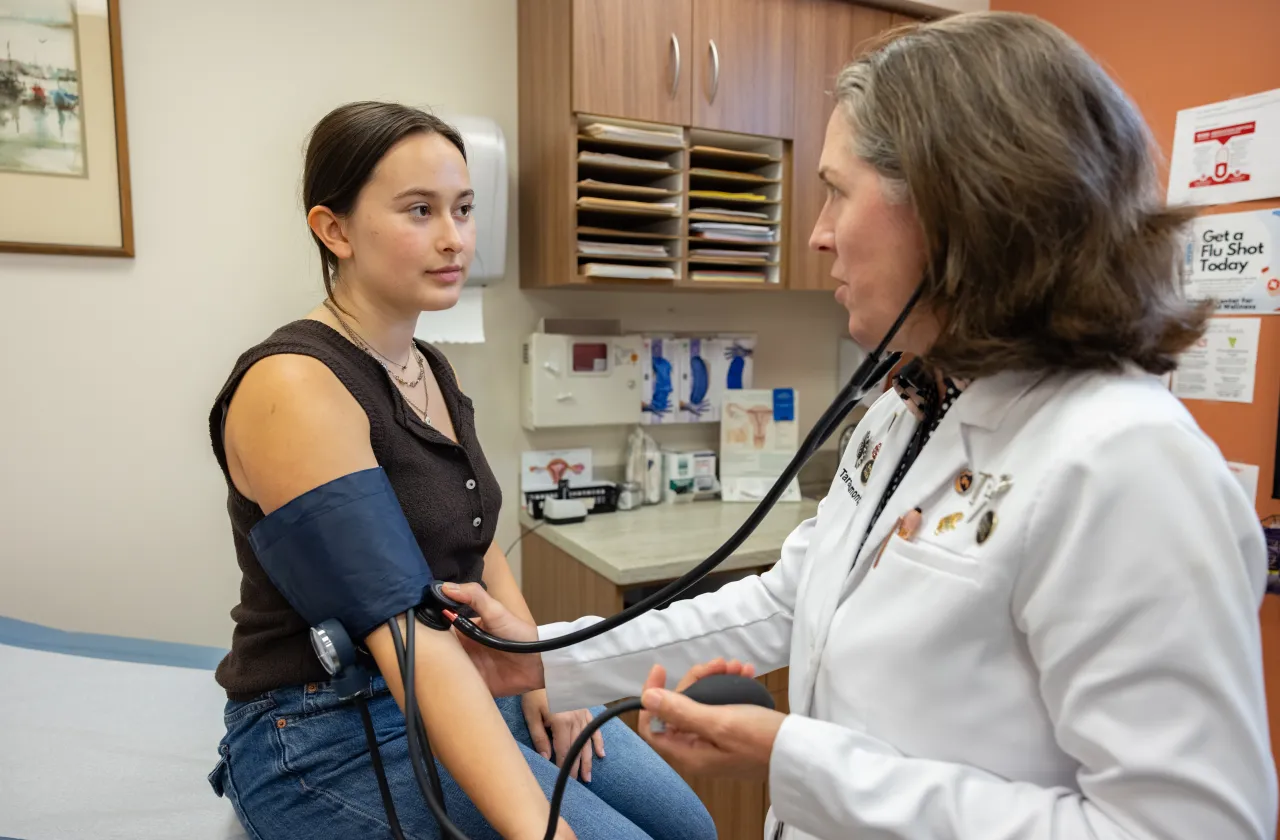 A doctor in a white lab coat takes the blood pressure of a student