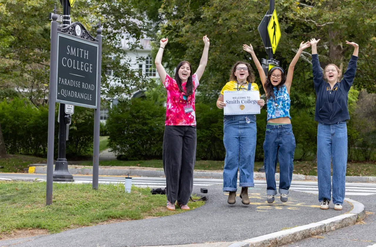 Students jump for joy next to the Quadrangle sign on move-in day 2025