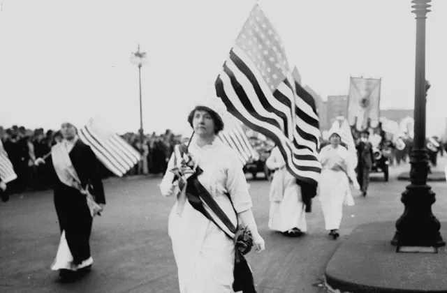 A woman in white carrying an American flag in the 1913 parade on Washington