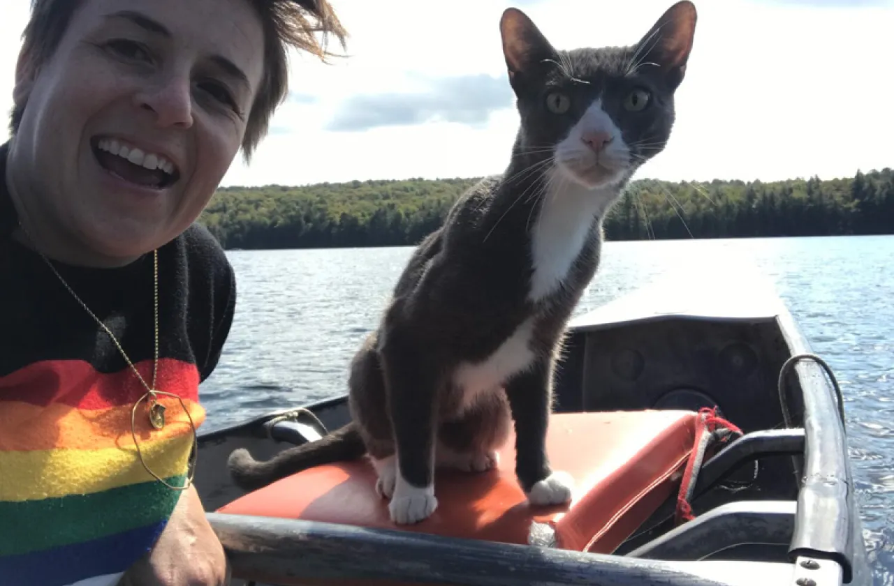 Winter Miller in a rainbow shirt with a gray and white cat on a boat in a lake.