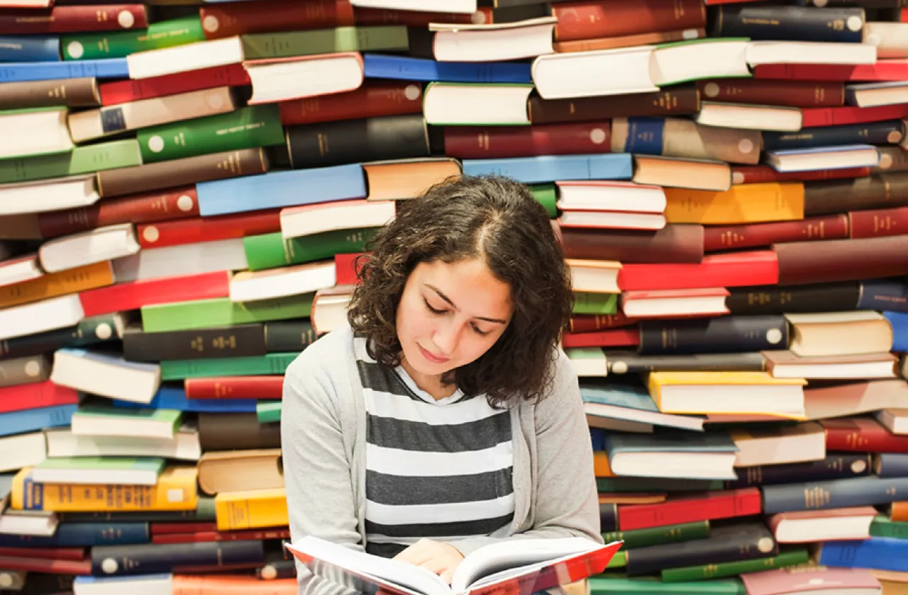 Student reading a book in front of piles of differently colored books