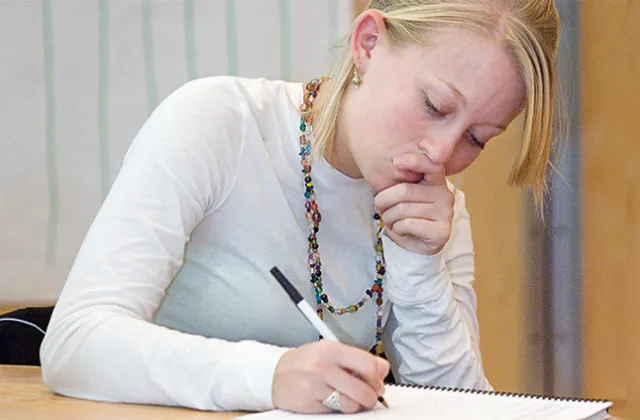 Student in white sweater writing in a notebook