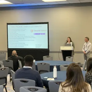 Emma Larsen presents research to a group while Alex Barron looks on.