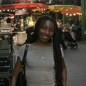 Portrait of Catherine Abilla smiling at an outdoor market with Borough Market signboards behind her.
