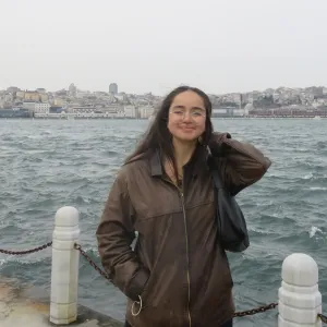 Isabella Grijalva smiling in a brown leather jacket in front of a wide body of water and a city skyline.