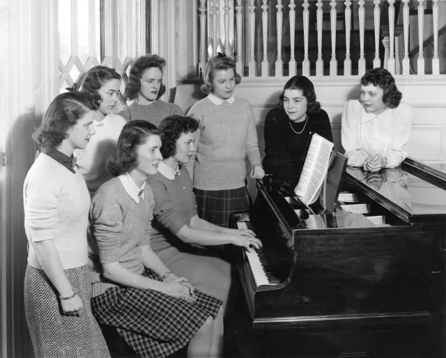 A group of students gathered around a piano in the 1940s.