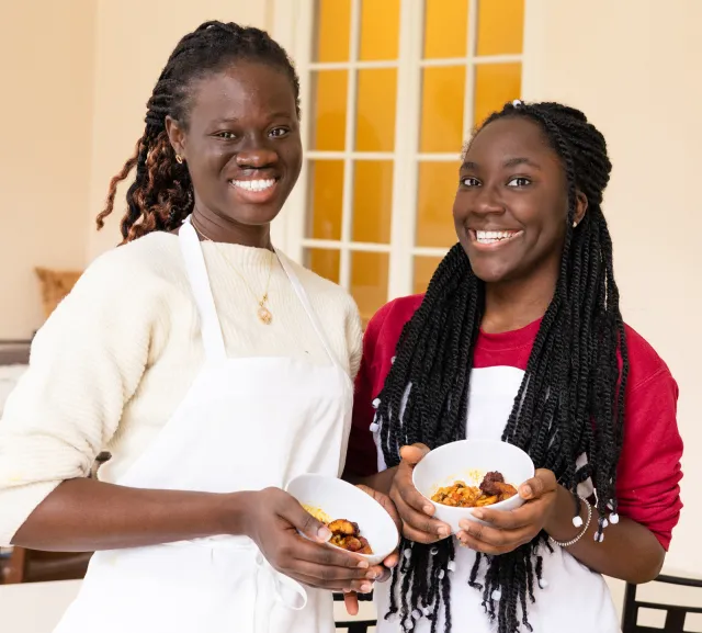 Two students in aprons smile holding a dish on IS Day