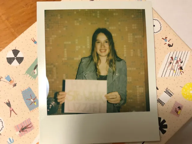 Polaroid of Violet Rawlings holding a sign "Happy Sib Week Lizzie!"