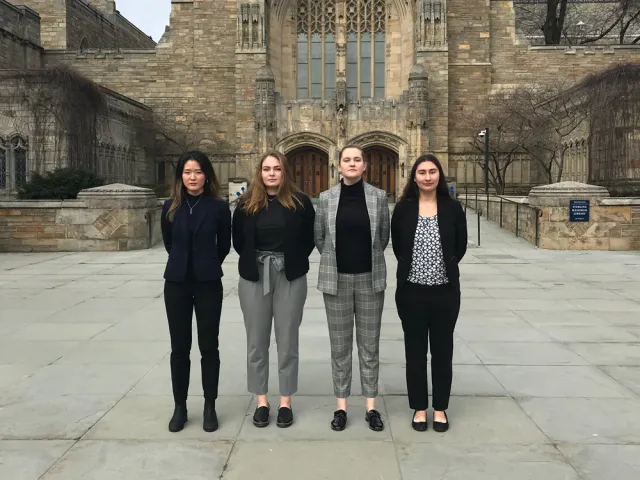 Four students in a line standing in front of Yale University's library