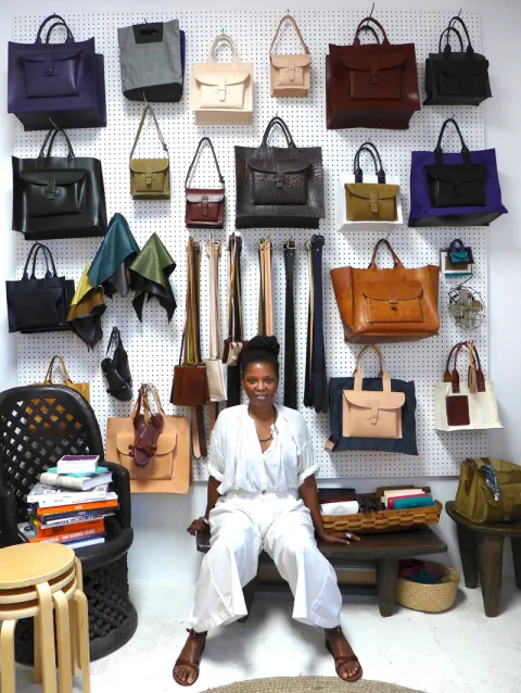 Agnes Baddoo seated with a wall of leather goods behind her