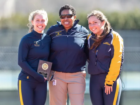 A coach with two track and field athletes, all smiling into the camera