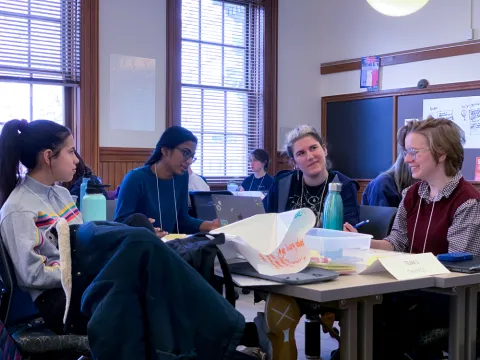 Group of four students, including people of color and a gender non-conforming student, doing group work