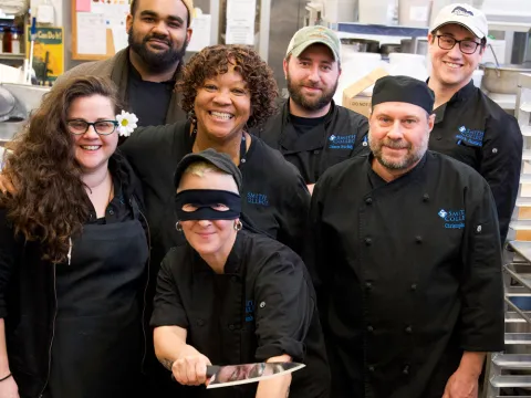 Group of dining services staff smiling at the camera. One is holding a cooking knife in mock battle.