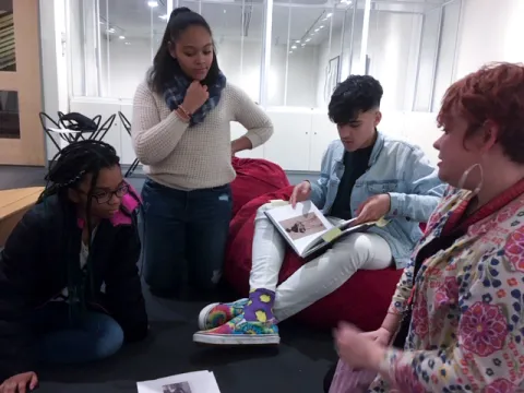 Three students of color looking at a copy of the exhibit book Black Refractions while an art educator looks on.