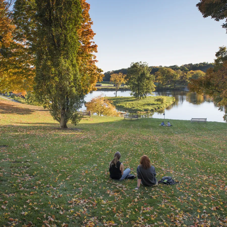 Two students sitting in front of Paradise Pond in the fall.