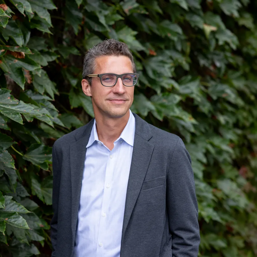 Tim Recuber stands in front of a wall of green leaves.