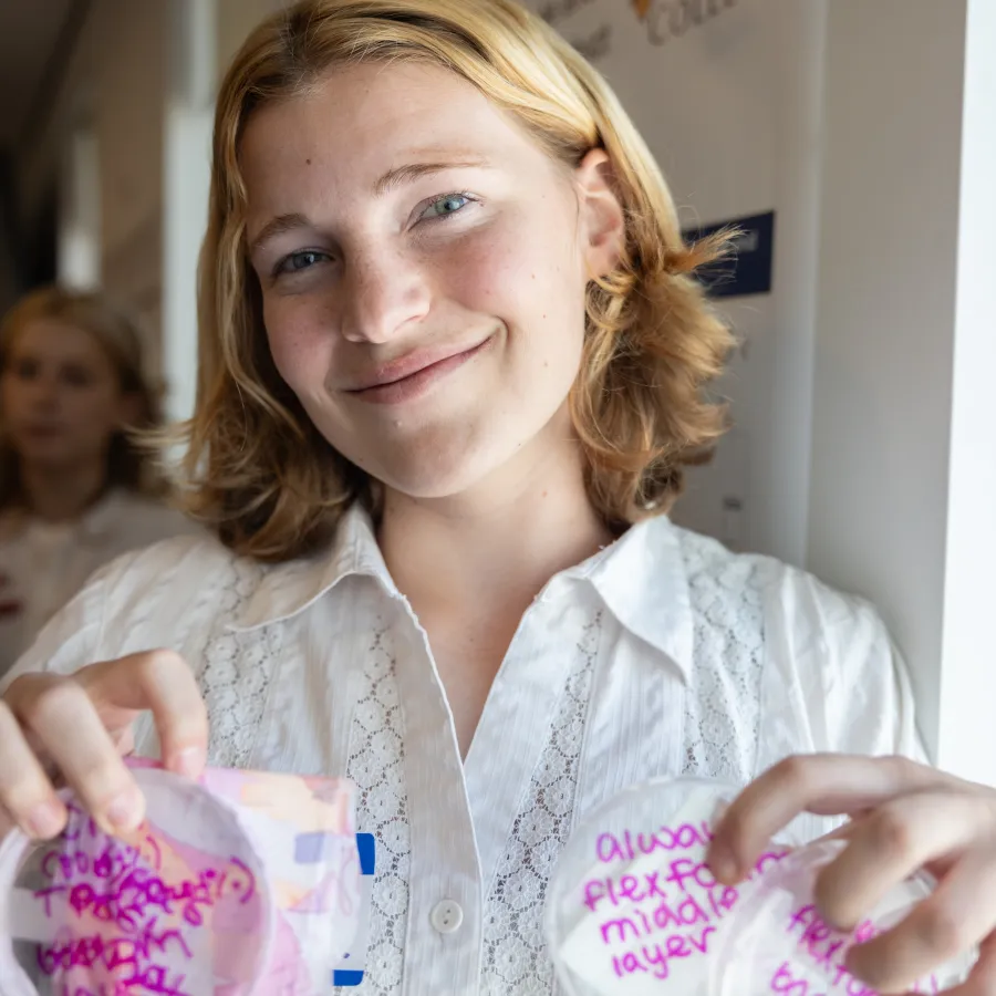 A student holds up several petri dishes with purple writing across the tops.