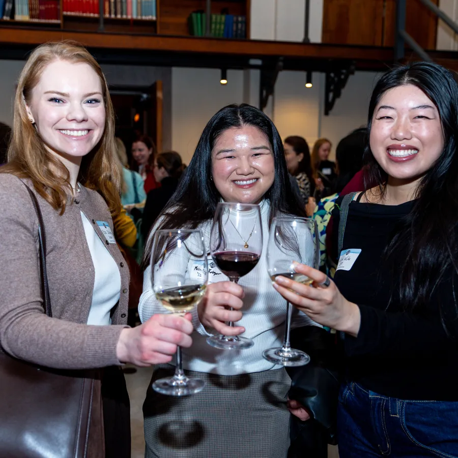 Three young alums smiling while toasting the camera