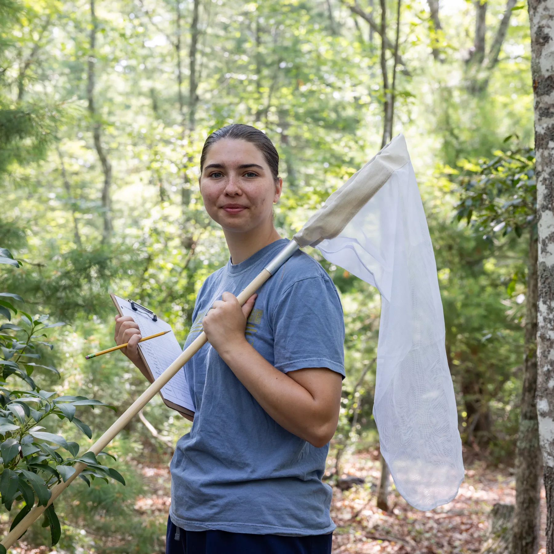 Chloe Dyehouse holds a clipboard and a large net in the woods of Rhode Island