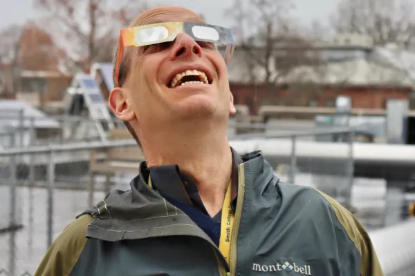 James Lowenthal wearing solar eclipse glasses looks up at the sky