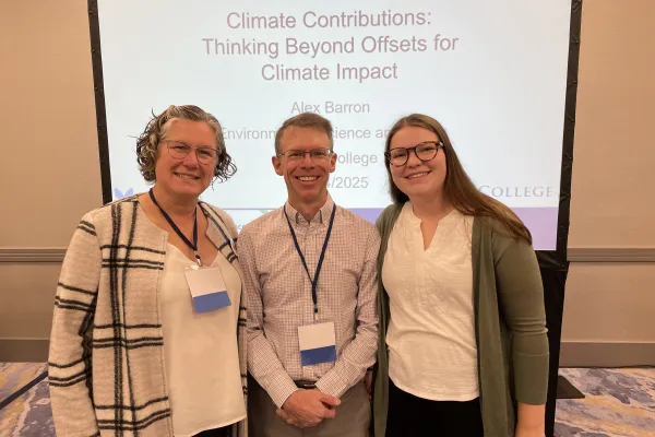 Becca Malloy, Alex Barron, and Emma Larsen pose for a photo in front of a projection screen.