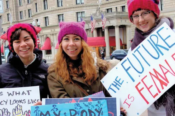 Three smiling people in pink pussy hats with signs including "The Future is Female"