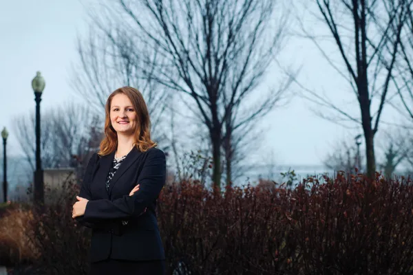 Aubrey Menarndt smiling with her arms crossed. Trees and bushes are immediately behind her and behind them is the open ocean