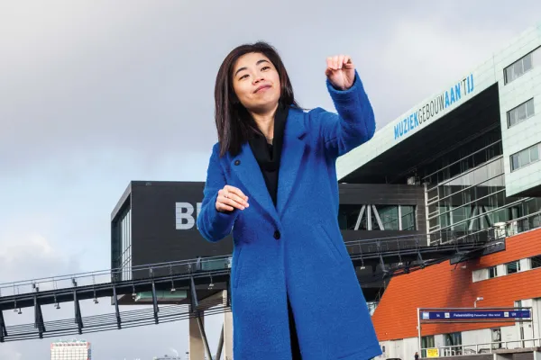 Elim Chan, who appears east Asian, in a bright blue coat and her hands in a conducting posture