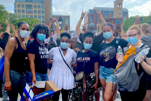 Six friends—five black and one white— in masks standing next to each other in front of a citscape. T-shirts include "Black Nerds Unite" and "Melanin Poppin"