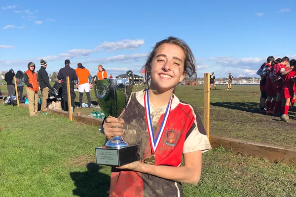Muddy Harriet Wright holding a rugby trophy